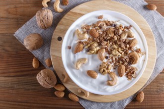 White plate with greek yogurt, granola, almond, cashew, walnuts on brown wooden background. top