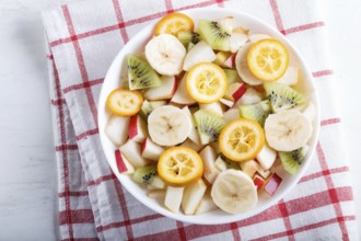 Vegetarian salad of bananas, apples, pears, kumquats and kiwi on linen tablecloth, top view, flat