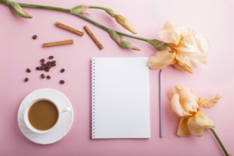 Orange iris flowers and a cup of coffee with notebook on pastel pink background. Morninig, spring,