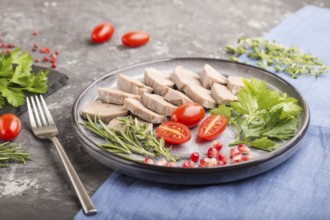 Boiled pork tongue with tomatoes and herbs on a black concrete background and blue linen textile.