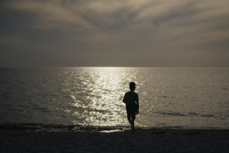 A child stands alone on the beach in the backlight of the setting sun. Born, 01.08.2024