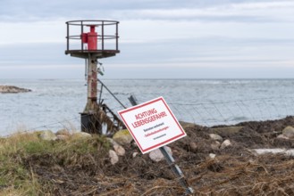 Beacon behind a fence with warning sign 'ACHTUNG LEBENSGEFAHR', cloudy sky over the sea, entrance