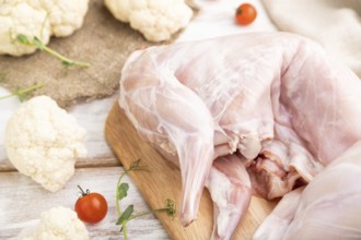 Whole raw rabbit with cauliflower, tomatoes and spices on a white wooden background and linen