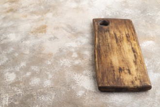 Empty rectangular wooden cutting board on brown concrete background. Side view, copy space