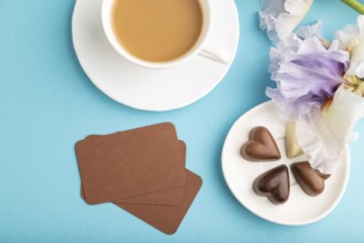 Brown business card with cup of cioffee, chocolate candies and iris flowers on blue pastel