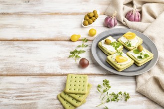 Green cracker sandwiches with cream cheese and cherry tomatoes on white wooden background and linen