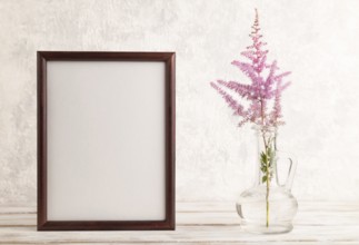 Wooden frame with pink astilbe flowers in glass vase on gray concrete background. side view, copy