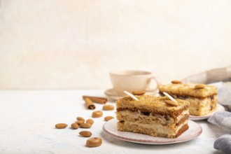 Honey cake with milk cream, caramel, almonds and a cup of coffee on a white concrete background and