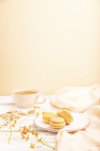 Orange macarons or macaroons cakes with cup of apricot juice on a white wooden background and