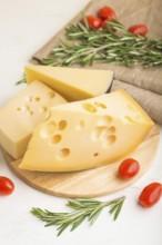 Various types of cheese with rosemary and tomatoes on wooden board on a white wooden background and