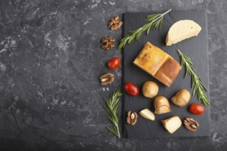 Smoked cheese and various types of cheese with rosemary and tomatoes on black slate board on a