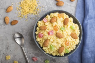 Millet porridge with candied fruits and almonds in blue ceramic bowl on a gray concrete background