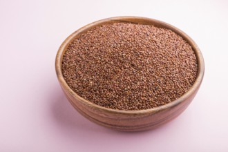 Wooden bowl with raw red quinoa seeds on a pastel pink background. Side view, close up