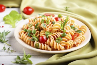 Fusilli pasta with tomato sauce, cherry tomatoes, lettuce and herbs on a white wooden background