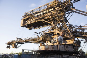 A man swings in front of an open-cast mining excavator illuminated by the evening sun at the Melt