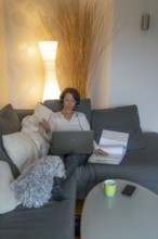 Woman, mid-50s, works from home, with laptop and communicates with colleagues via headset, home