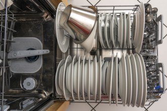 Dishwasher, full, with cleaned crockery, cutlery, cooking utensils