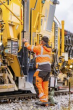 A worker interacts with large yellow machines on a railway line, track construction Hermann Hesse