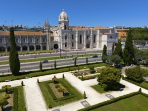 Gothic church with surrounding gardens and green areas next to a street under a clear blue sky,