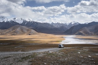 Off-road vehicle on a gravel track, glaciated and snow-covered peaks, Ak Shyrak Mountains, near