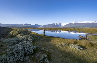 Tourist standing at the lakeshore, reflection in a lake, view of glacier tongues Skaftafellsjökull