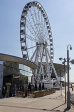 Large Ferris wheel next to a modern building in an urban space, Liverpool