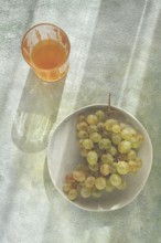 A branch of white grapes, on a gray plate, with a glass of white wine, top view, natural light,