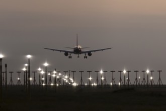 Airbus jet passenger aircraft on approach to land at sunset over landing lights, London Stansted