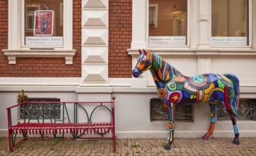 Colourful horse sculpture in the style of pop art and a red bench in the city of horses Warendorf,