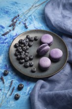 Purple macarons or macaroons cakes with blueberries on ceramic plate on a blue concrete background