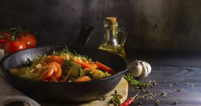 Frying pan with healthy vegetables and a bottle of oil on a rustic wooden table. The vegetables