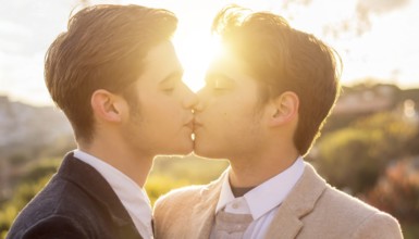 Two men kissing each other in a field. Scene is romantic and intimate. The idea behind the image is