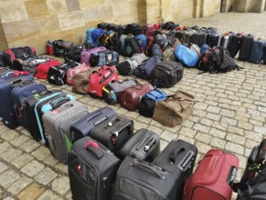 The luggage of a group of travellers stands in rows on the pavement, outside, suitcases and bags