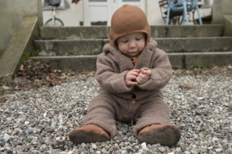 Small child, 8 months, wrapped up warm, sitting on the gravel and playing with stones,