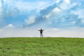 View of a backpacker man spreading his arms on a hill. Successful backpacker on top of a hill