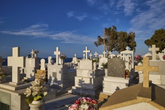 A peaceful cemetery with numerous white gravestones and crosses stretching down to the sea, Agios