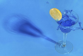 A splashing blue drink with a slice of lemon casts shadows on a blue background