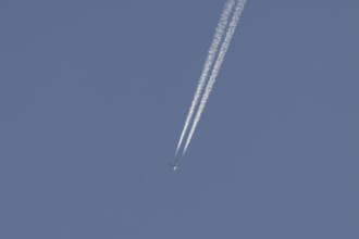 Jet aircraft flying across a blue sky leaving a contrail or vapor trail in the atmosphere behind