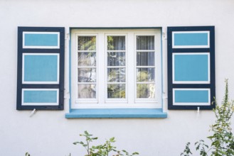 Detailed view of a historic white window with blue shutters in a white wall, artists' village