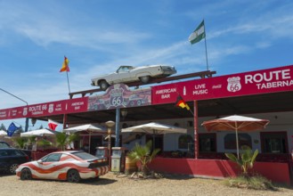 A Route 66-style retro taberna with flags, cars and parasols under a blue sky, Tabernas Desert,