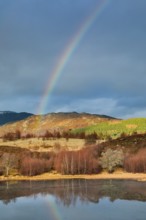 Atmospheric cloudy sky with rainbow over mountainous, partly wooded Highlands in the west of