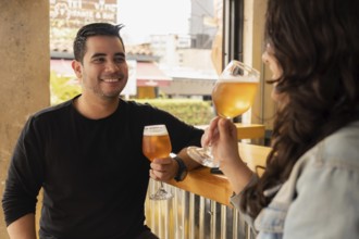 Smiling young man and woman enjoying a refreshing glass of beer at a daytime bar. The casual and