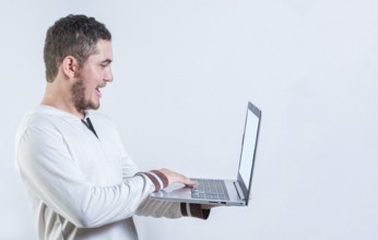 Portrait of happy young man standing using laptop isolated. Excited guy holding and looking at an