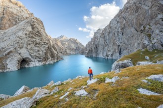 Young man at the turquoise mountain lake Kol Suu with rocky steep mountains, Kol Suu Lake, Sary