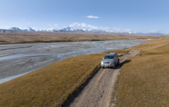 Off-road vehicle on gravel track, mountain valley with meandering river, barren dramatic mountain