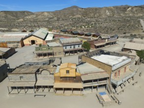 Western town with wooden houses and a dry, mountainous landscape on a sunny day, aerial view, Fort