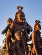 Traditional Himba woman with baby on her back, portrait, in the evening light, near Opuwo,