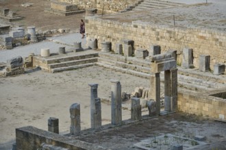 Ruins of an ancient temple with stone columns and a visitor near stone walls, Kamiros,