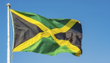 The flag of Jamaica flutters in the wind, isolated against a blue sky