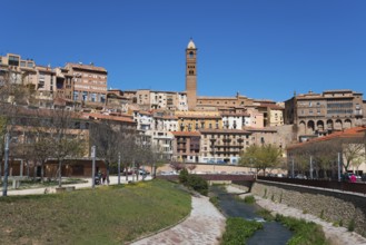 Historic town with a central stone tower, river in the foreground and several residential buildings